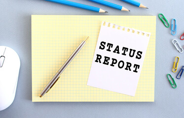 STATUS REPORT is written on a piece of paper that lies on a notebook.