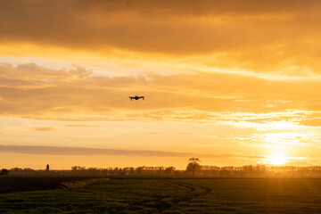 drone flying over green springtime meadows with a colorful orange sunset sky behind