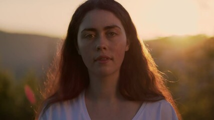 Portrait of young smiling woman draping an American flag over her shoulders. Sunset sky in the background. Slow motion. Dolly shot. The concept of American National Holidays.