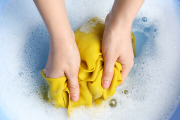 Top view of woman hand washing color clothing in suds, closeup