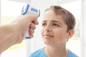 Doctor checks boy's body temperature using infrared forehead thermometer for symptoms of Coronavirus or other infections