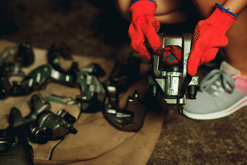 A girl in orange gloves holds a car brake caliper at a service station.