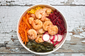 Top view of a poke of prawns, nori, corn, carrots, radishes and beets.