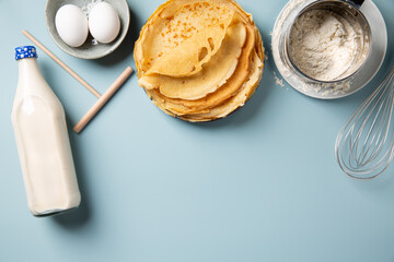 Stack of homemade crepes and ingredients for making thin pancakes around on blue background. Top view, copy space.