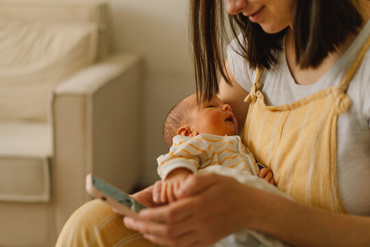 Mother sitting on bed and typing on the cellphone while son is napping.