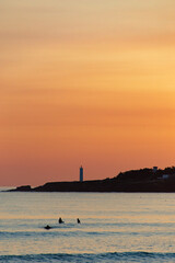Surfers enjoying sunset in french westcoast, lighthouse and waves, amazing colors