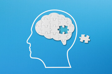 Brain shaped white jigsaw puzzle on blue background, a missing piece of the brain puzzle, mental health and problems with memory
