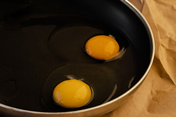 One raw egg in a black frying pan on a paper. Transparent white and bright round yellow yolk. The concept of the process of cooking a simple dish for breakfast. Close-up. Top view