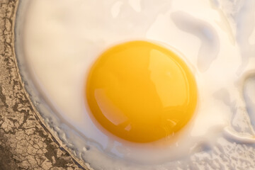 One bright round raw yolk in finish white with edge cracks in a dark skillet. Cooked small fried eggs is a simple breakfast. Top view, close-up