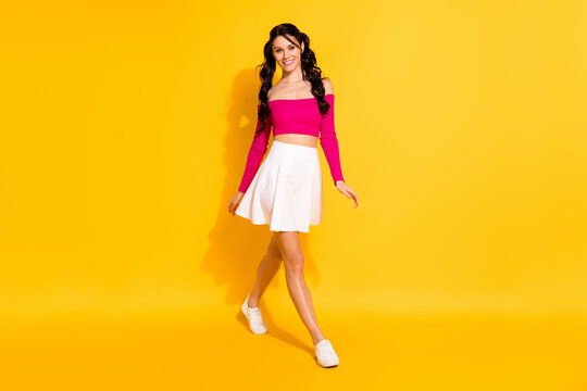 Full length photo of charming pretty young woman wear pink top white skirt walking isolated yellow color background