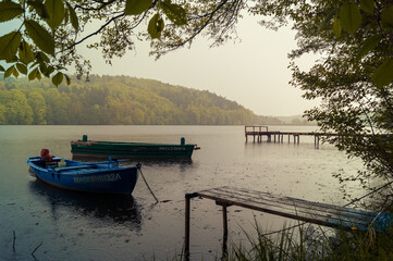 Naklejka na ściany i meble Dwie łodzie oraz pomost na tle jeziora w Łapinie w pochmurny deszczowy dzień.