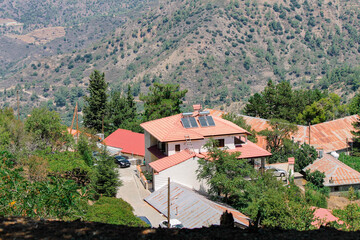 Fototapeta na wymiar Roofs of Kykkos monastery between green trees on a clear sunny day