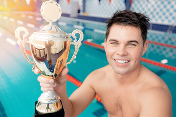 Young man winner in swim pool with champion gold trophy with sun light