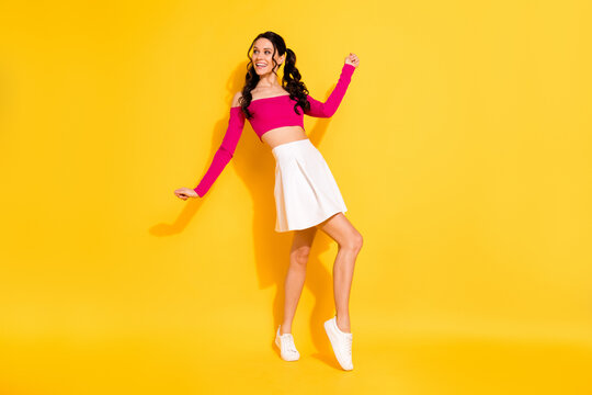Full length photo of funny shiny young woman wear pink top white skirt dancing looking empty space isolated yellow color background