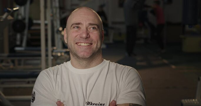 Paralympian man with defective legs sitting in a wheelchair in the gym looking at the camera smiling