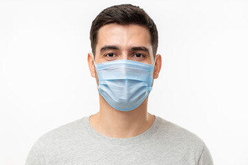 Young handsome man wearing t-shirt and medical mask, standing isolated on gray background