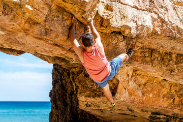 A rock climber safely climbing a yellow cliff in Algarve, Portugal - obrazy, fototapety, plakaty