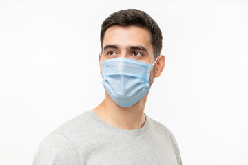 Young handsome man wearing t-shirt and medical mask, standing isolated on gray background, looking away