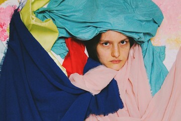 artistic portrait of young woman with serious angry face in colorful textile fabrics
