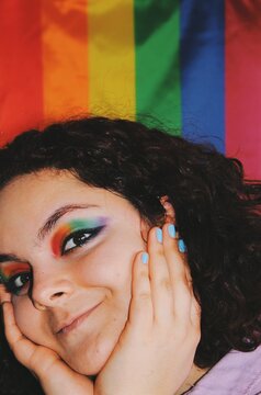closeup smiling happy portrait of queer young woman with lgbtqia+ pride flag eye makeup and spectrum colors of lgbtq pride flag in background - eyes opened version