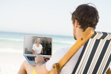 Caucasian man relaxing on beach having video call using laptop