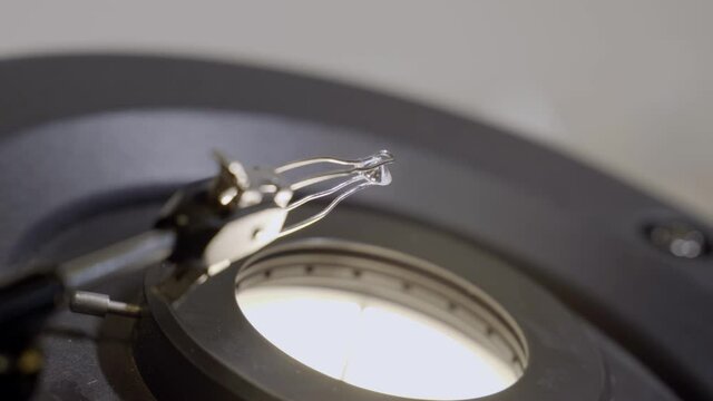 Small classic round diamond is held next to microscope to be examined and clean. In diamond or gemology laboratory a shiny diamond is being checked for value and grading to set price for sale or trade