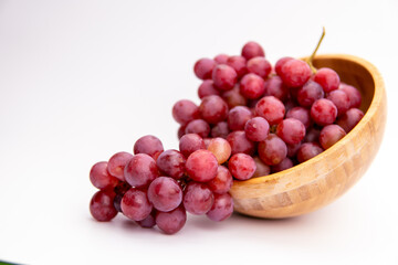 Red grapes in a wooden bowl isolated on white background. Fresh bunch of fruits. Selective focus
