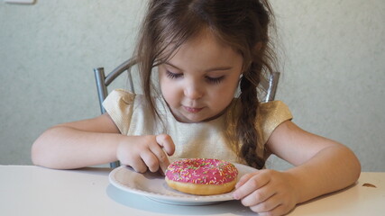 Little happy cute girl is eating donut. child is having fun with donut. Tasty food for kids. Funny time at home with sweet food. Bright kid. Donut with chocolate.