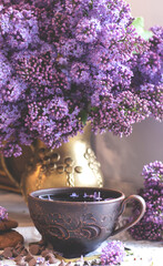 Decorative composition with a Bouquet of lilacs. Clay cup of tea and chocolate cake. A bouquet of lilacs in a vase. Spring floral background with lilacs in the interior. 