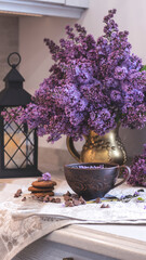 Decorative composition with a Bouquet of lilacs. Clay cup of tea and chocolate cake. A bouquet of lilacs in a vase. Spring floral background with lilacs in the interior. 