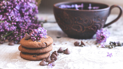 Decorative composition with a Bouquet of lilacs. Clay cup of tea and chocolate cake. A bouquet of lilacs in a vase. Spring floral background with lilacs in the interior. 