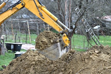 A road excavator digs soil on the foundations of an outbuilding to the house