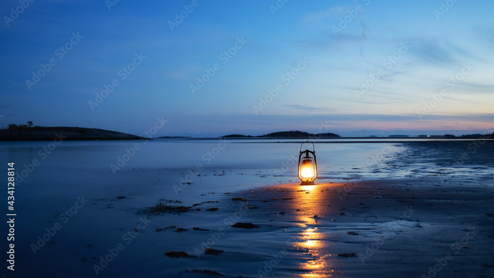 Wall mural Vintage oil lamp on the sea at sunset. Oantern burning with an orange soft flame. Blurred background.
 - Wall murals