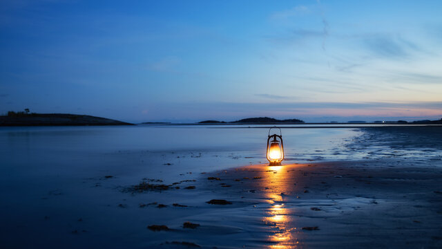 Vintage oil lamp on the sea at sunset. Oantern burning with an orange soft flame. Blurred background.
