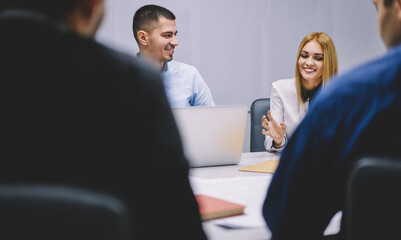 Happy red hair woman in smart casual wear communicate with male partners sitting at desktop with digital computers, successful business persons have brainstorming collaboration in office workspace