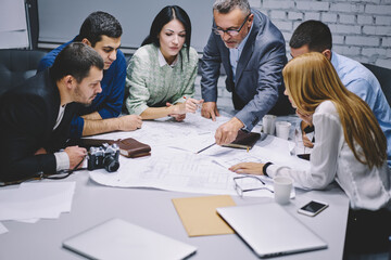 Crew of professional architects have productive collaboration completing sketch for project together, experienced designers developing paper blueprint checking details during briefing teamwork