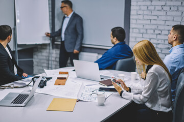 Female employee using cellphone device for browsing website and make online booking and banking while male colleagues analyzing project details and business strategy, collaboration and brainstorming