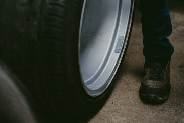 Car tire being rolled on the ground in a workshop with a leg of a worker showing