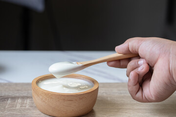 White yogurt in a wooden cup with a wooden spoon