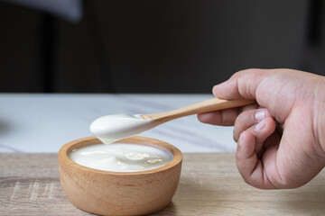 White yogurt in a wooden cup with a wooden spoon