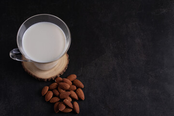 Obraz na płótnie Canvas Fresh almond milk in a clear glass and almond kernels on a black background.