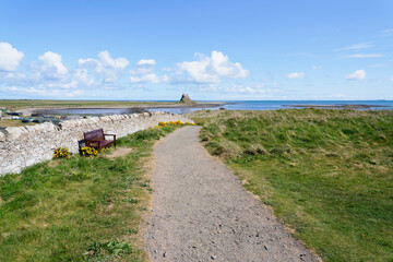 Fototapeta na wymiar Footpath beside a stone wall leading to a distant Lindisfarne Castle