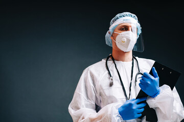 Young man nurse hospital worker in medical protective mask, gloves and protective wear isolated on dark background with copy space.