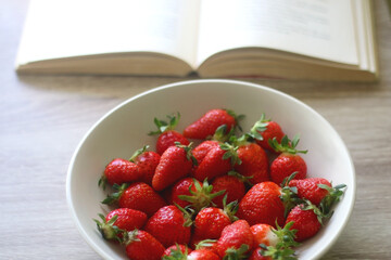 Bowl of strawberries and open book on a table. Selective focus.