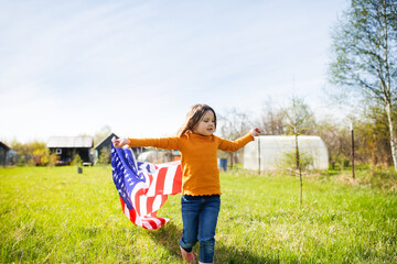 Happy American kid girl with waving USA flag on independence day. Child running with the USA flag at a picnic on July 4th