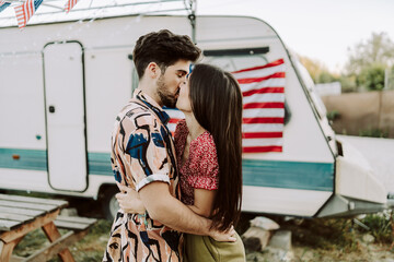 Pareja besándose frente a una caravana con una bandera de estados unidos