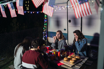 Grupo de amigos comiendo barbacoa por el día de la independencia de estados unidos de américa junto a una caravana con la bandera americana