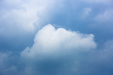 Obraz premium Single fluffy cumulus cloud among dark blue toned rain clouds forming a thick pack background with various shades. Climate and weather conditions. Scientific nature concept.