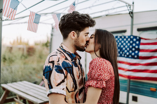 Pareja de chico y chica juntos besandose con la bandera de estados unidos de fondo en una caravana