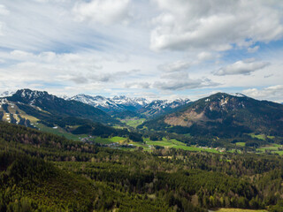 Snowy mountains of the Allgäuer Alpen by aerial - drone view on a party cloudy and sunny day with green trees on the foreground